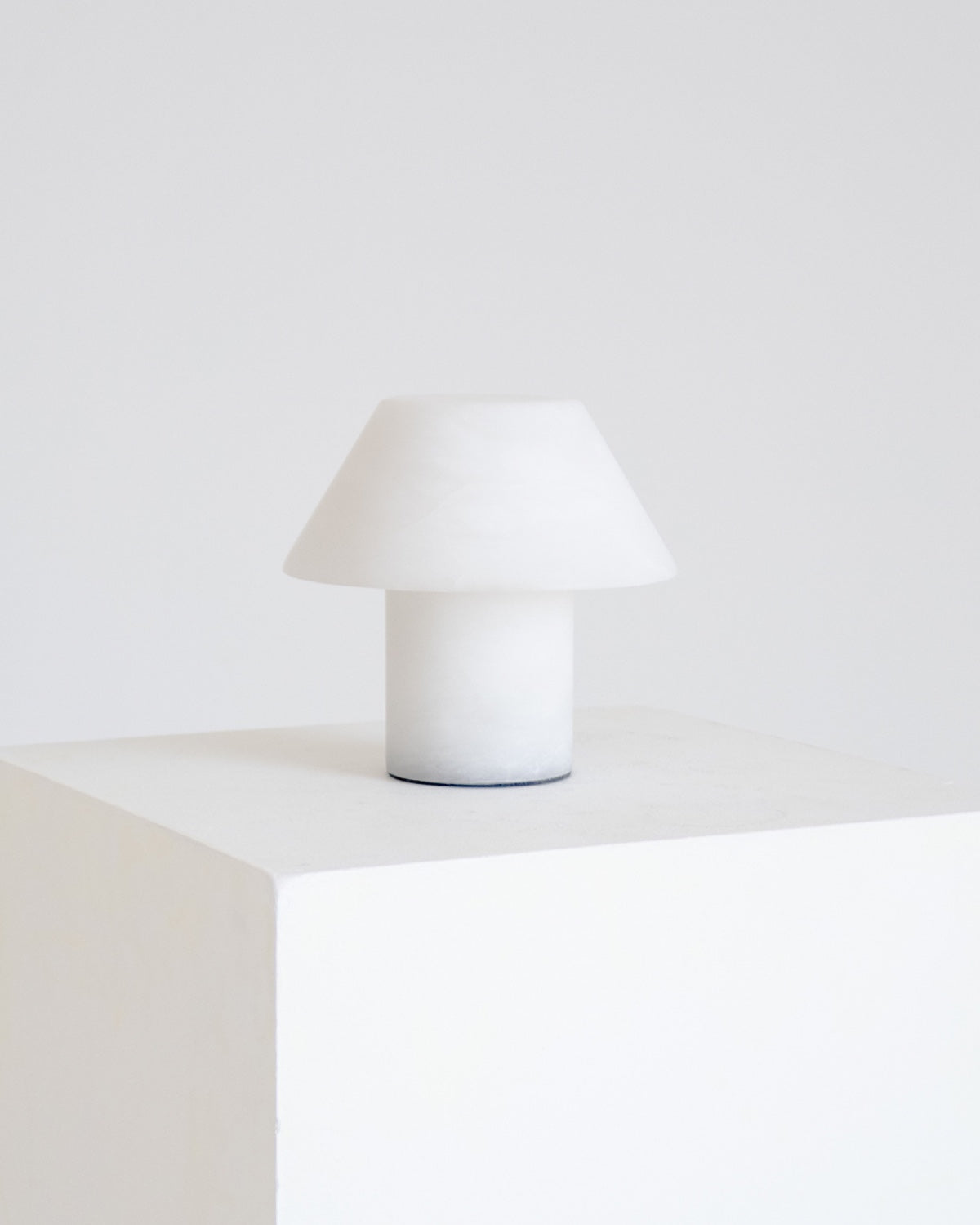White table lamp with fabric cone shade and cylindrical base, centered on a platform