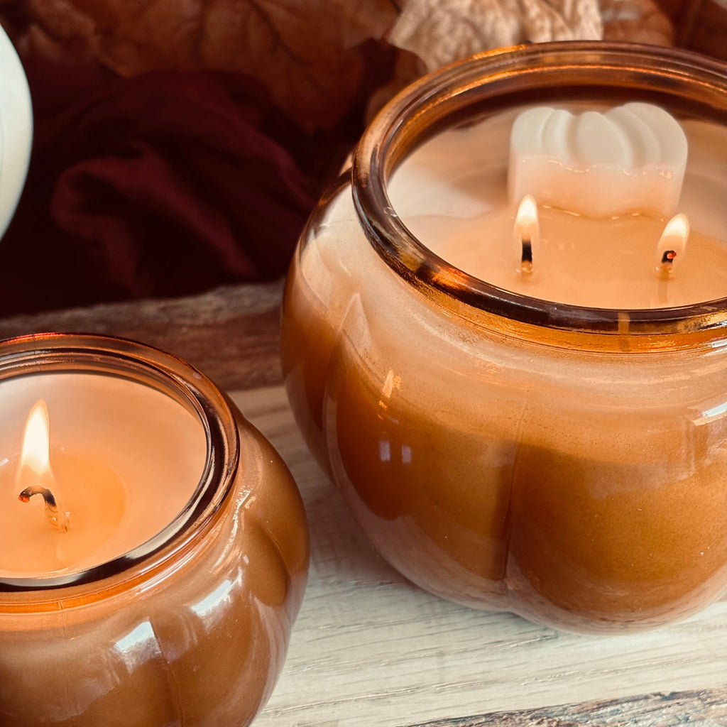 Two amber soy candles in round glass jars with lit wicks and white wax tops