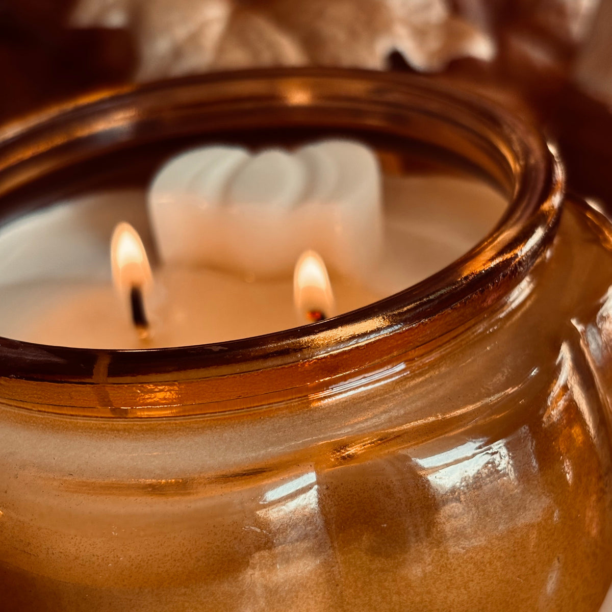 Close-up amber soy candle flame and white wax ridges inside round glass jar