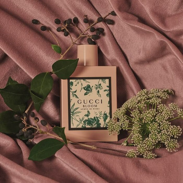 Pink perfume bottle with Gucci Bloom label on mauve fabric with green leaves