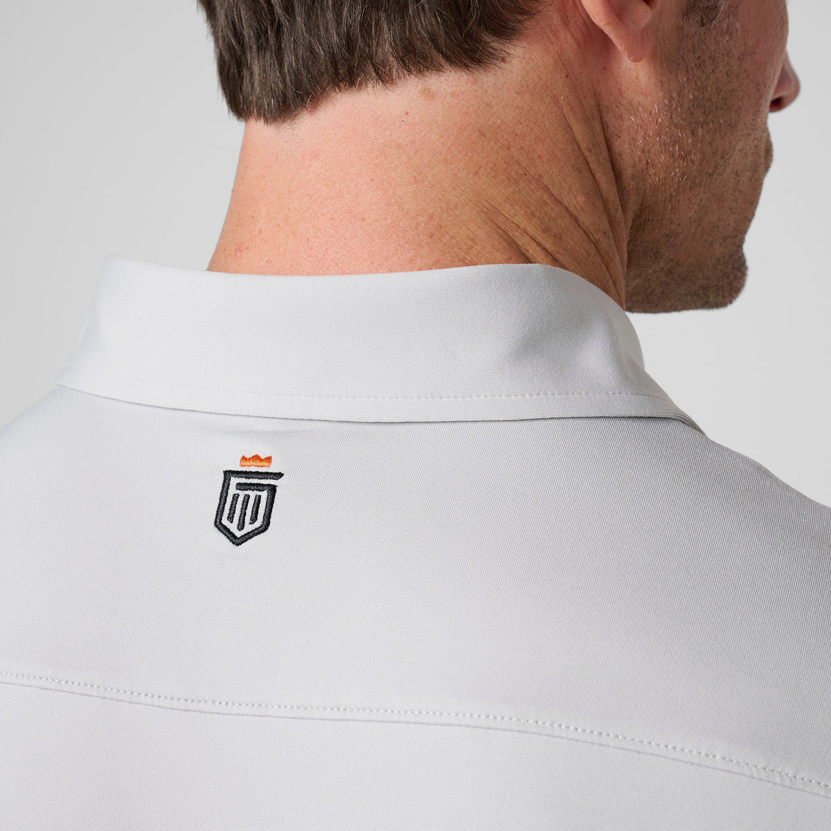 Ash gray polo back collar with small shield logo near the neckline.