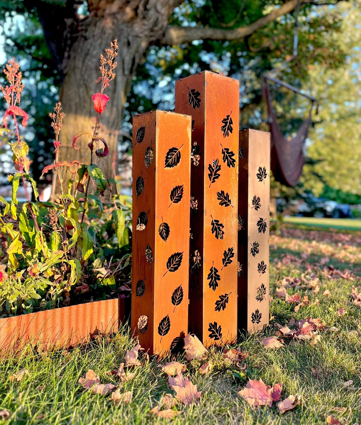 Orange and rust solar pillar luminaries with leaf cutout designs on metal posts
