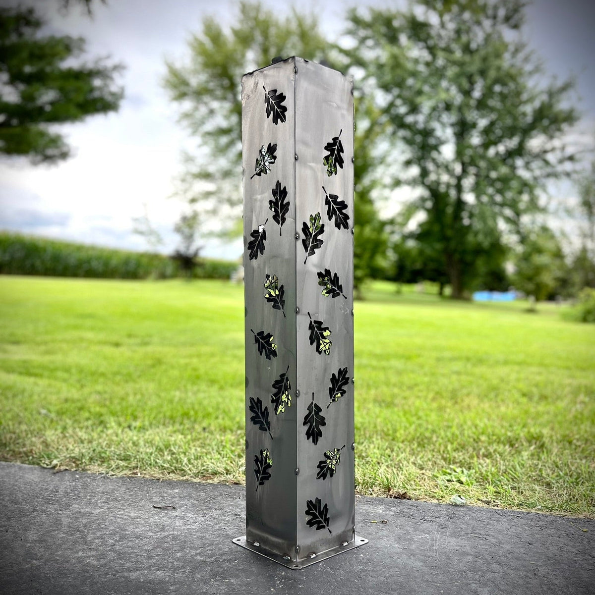 Light gray solar pillar luminary with black leaf cutouts and metal base plate