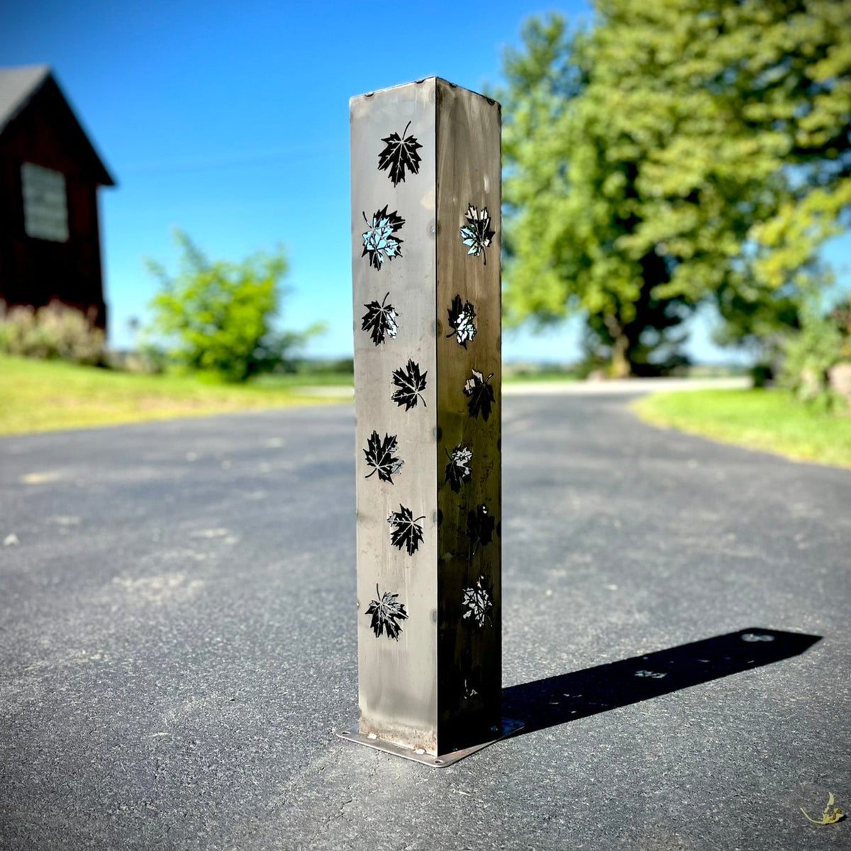 Light gray solar pillar luminary with leaf cutout pattern on tall metal panel
