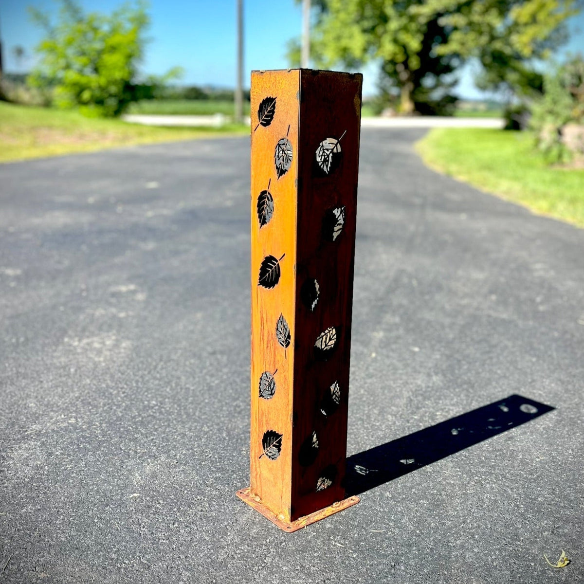 Orange and rust solar pillar luminary with leaf cutout pattern on metal frame