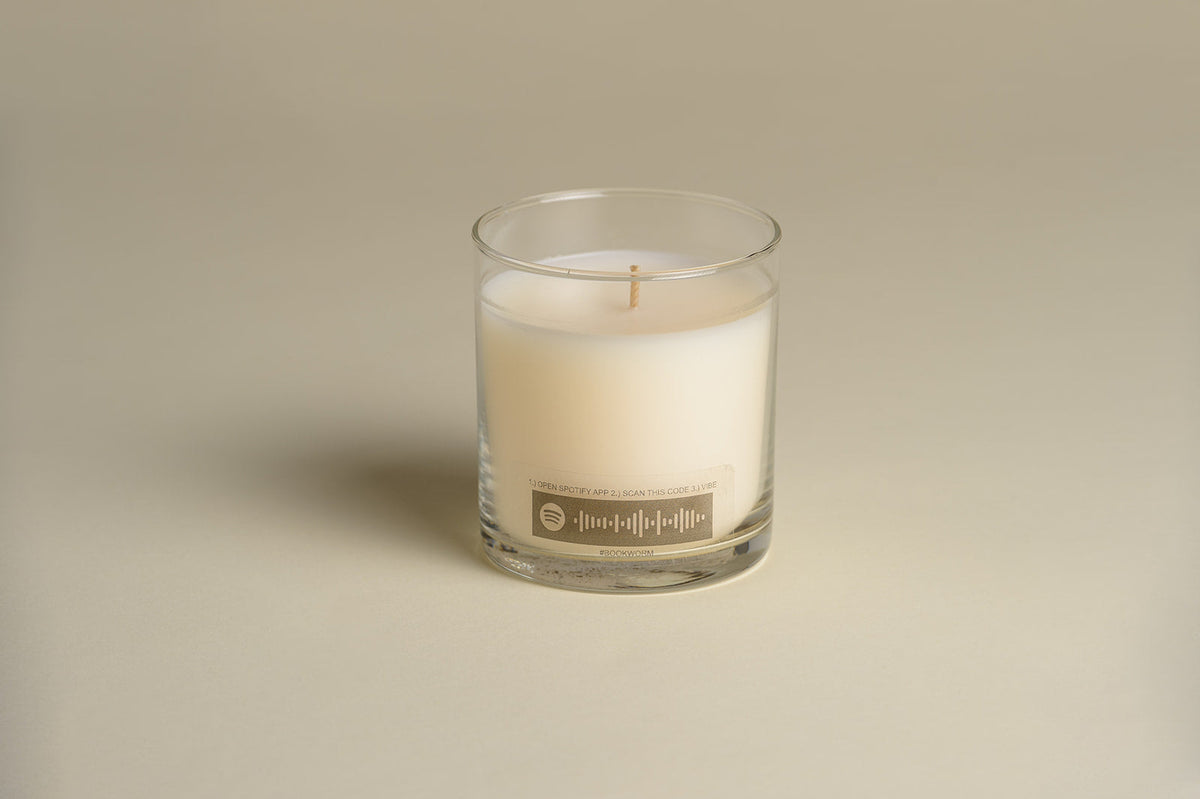 Luxury candle in clear glass jar with white wax and visible wick, front label on jar.