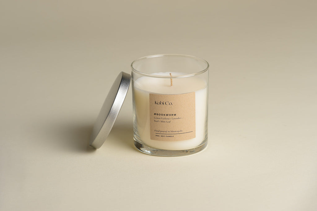 Bookworm luxury candle in clear glass jar with white wax and small wick; lid beside it.