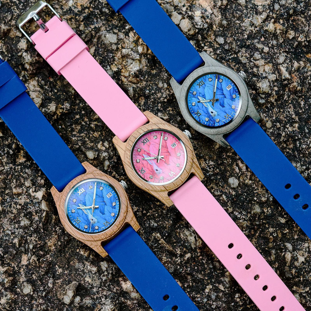 Three women’s wood wristwatches with blue/pink silicone straps and round blue/pink dials.