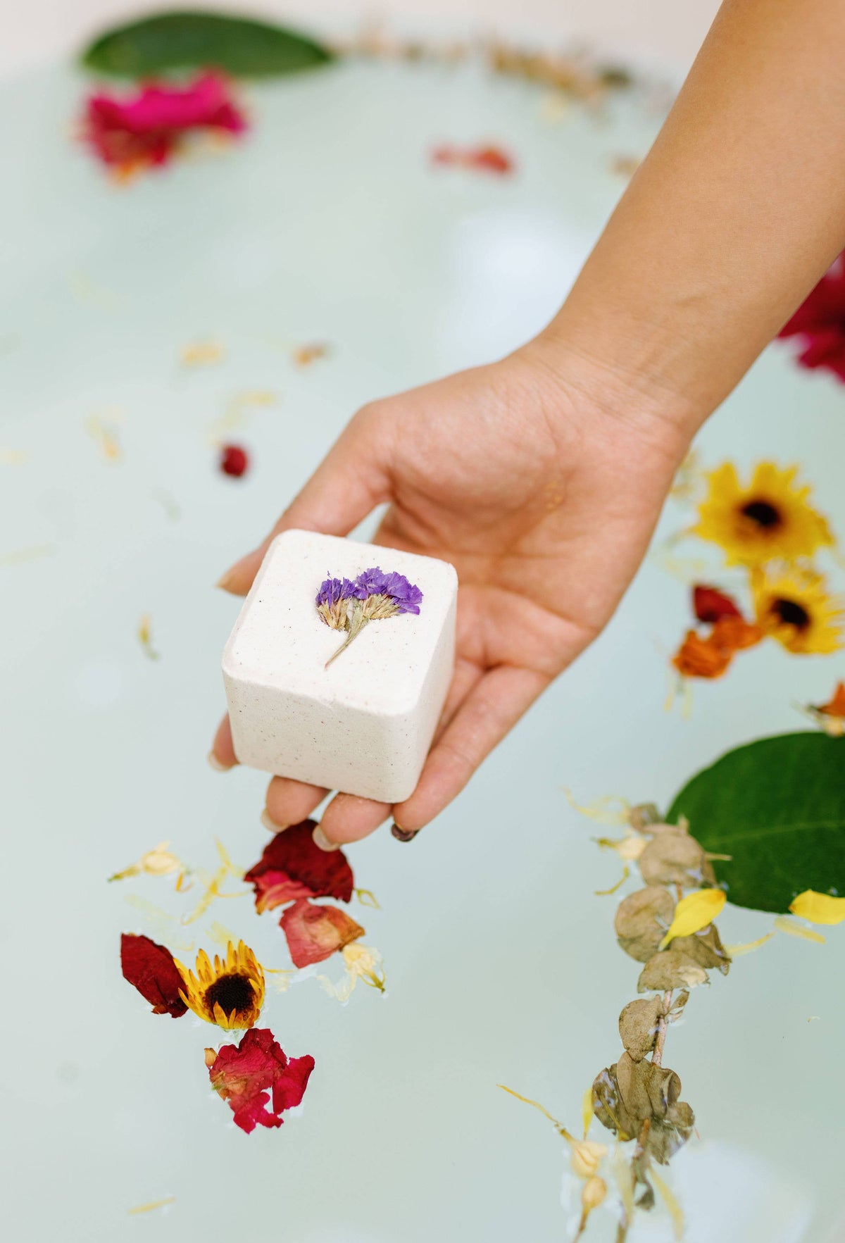 Square bath bomb cube in hand, white with a purple dried-flower top