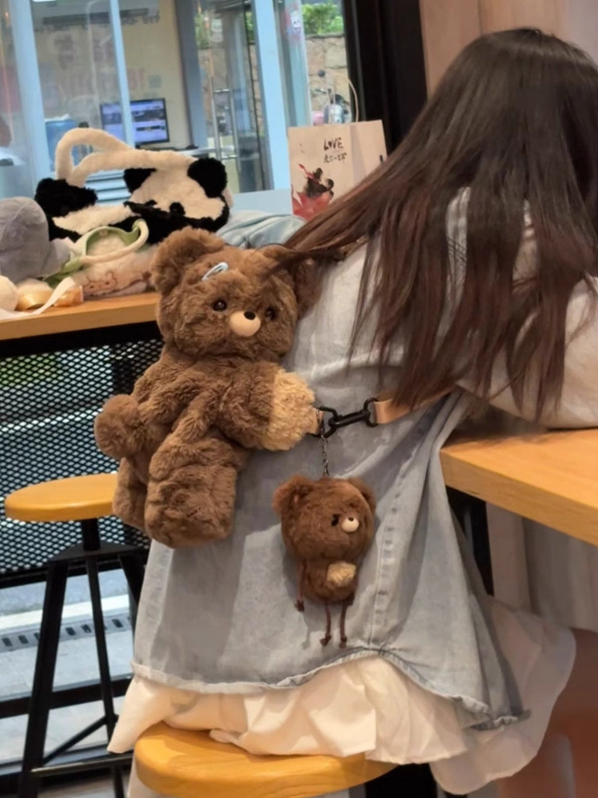Brown plush teddy bear backpack bag held by straps with front teddy plush and charm bear
