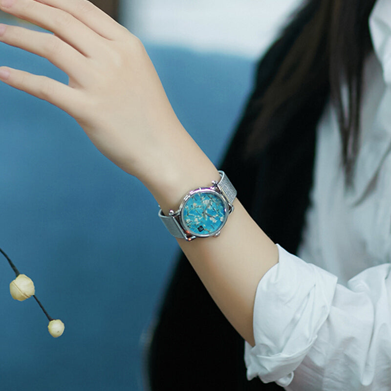 Women's quartz watch on wrist with turquoise leather band and teal floral face.