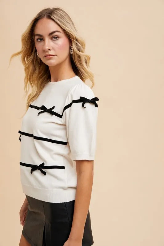 White knit top with black striped bands and bow details on short puff sleeves