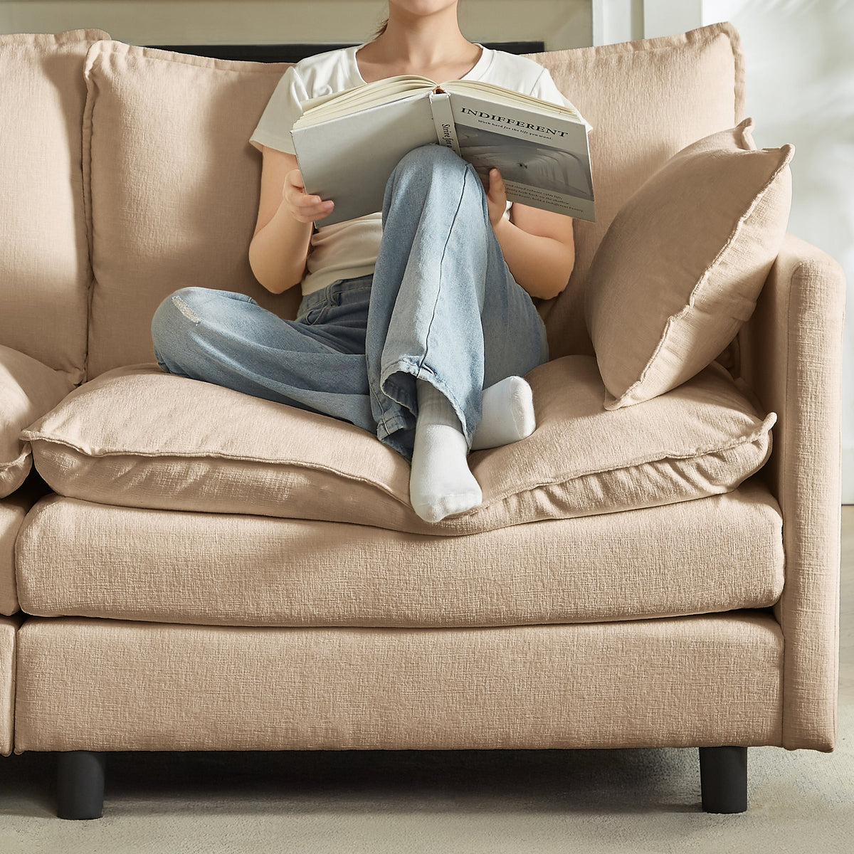 Beige sofa with three back pillows; person lounging and reading on the cushion.