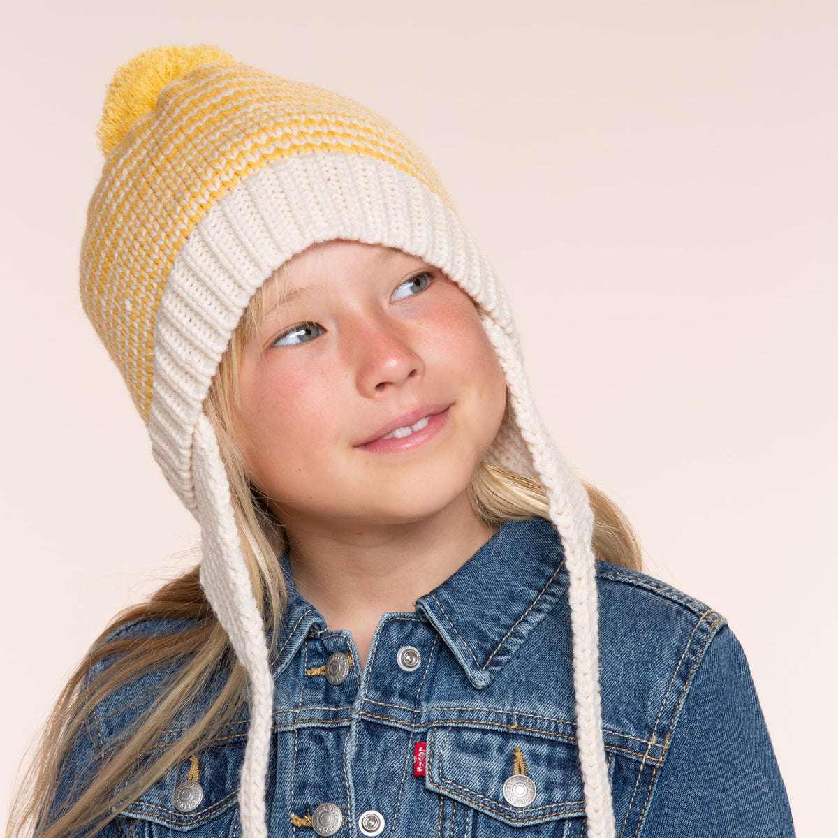 Yellow striped knit earflap beanie with pom-pom and tie strings on a child.