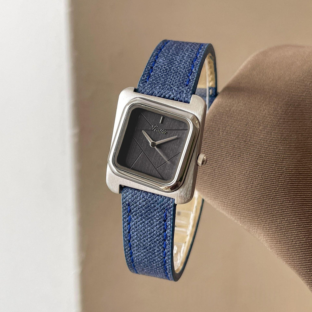 Square quartz watch with silver case, blue strap, and dark dial