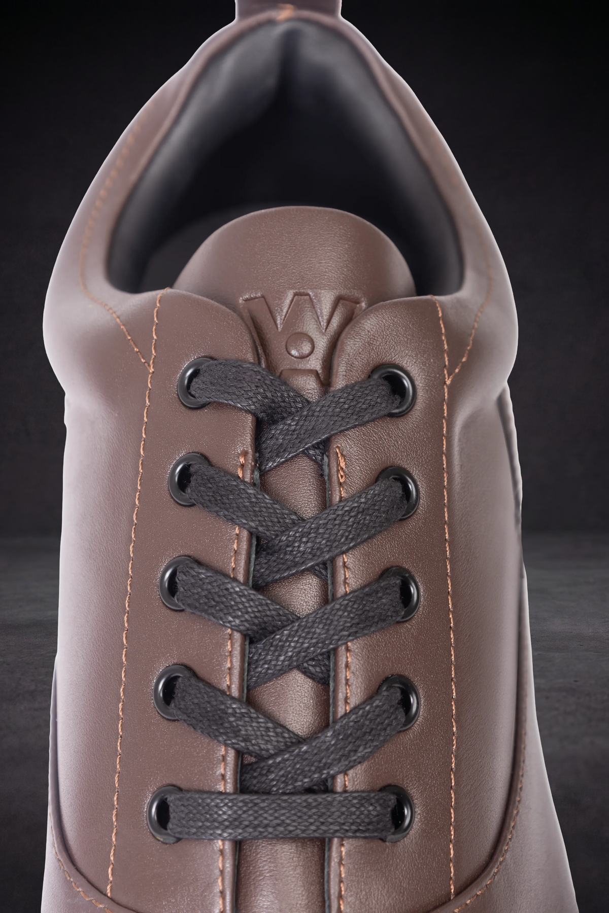 WOA brown sneaker close-up with black laces, eyelets, and cushioned tongue
