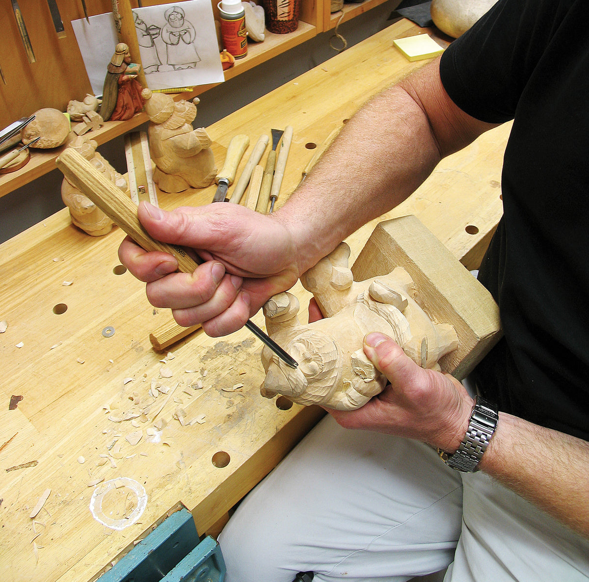 Woodworking hands carving a wooden angel plaque with chisels and figurine pieces