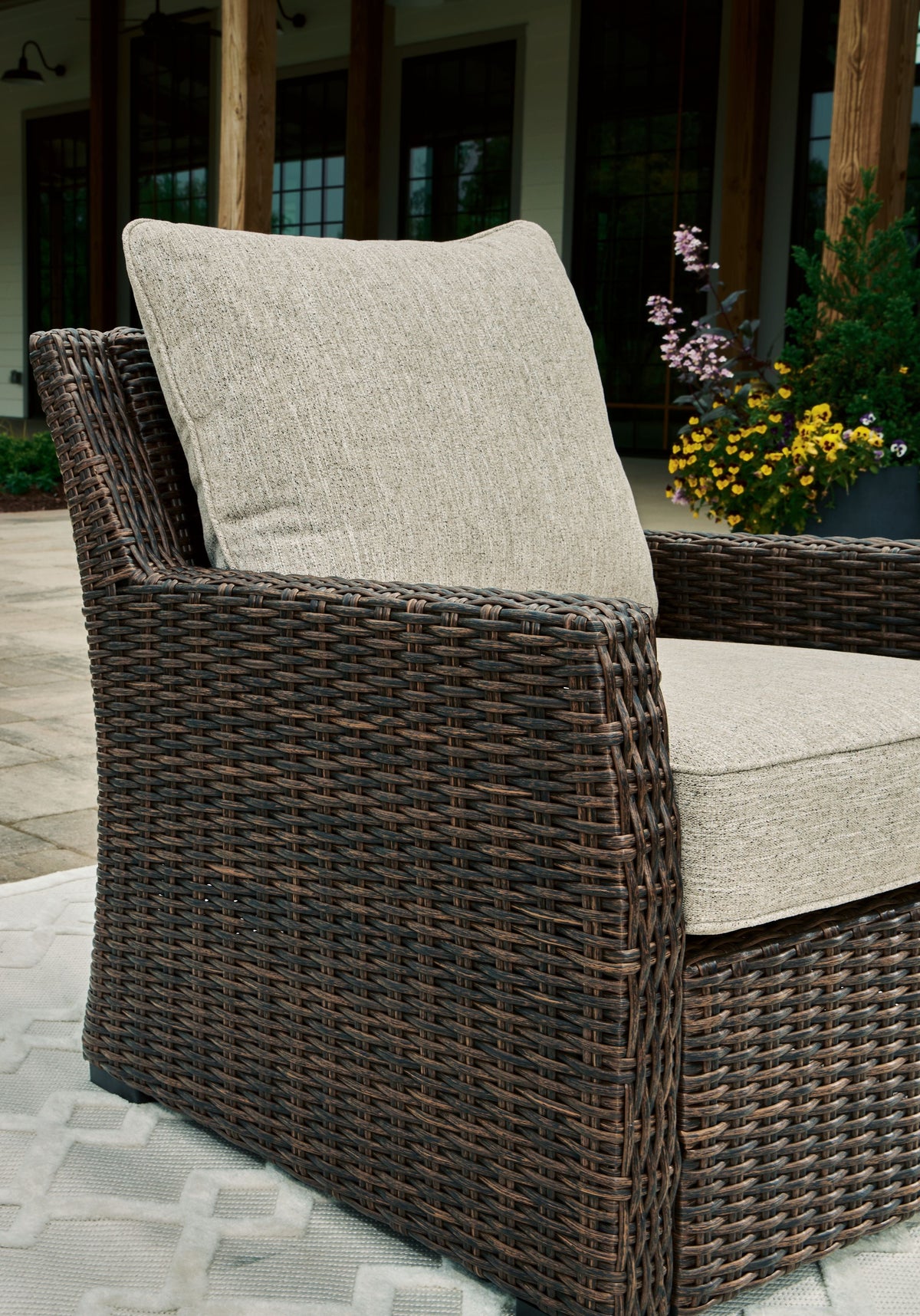 Brown woven lounge chair with beige seat cushion and back pillow