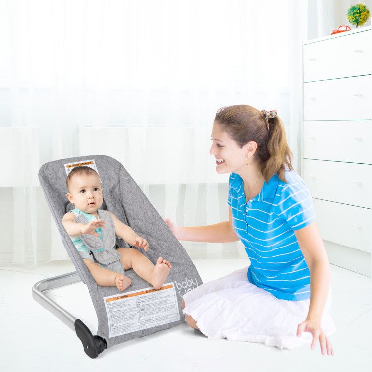 Gray baby bouncer seat with 5-point harness, baby reclining while caregiver adjusts