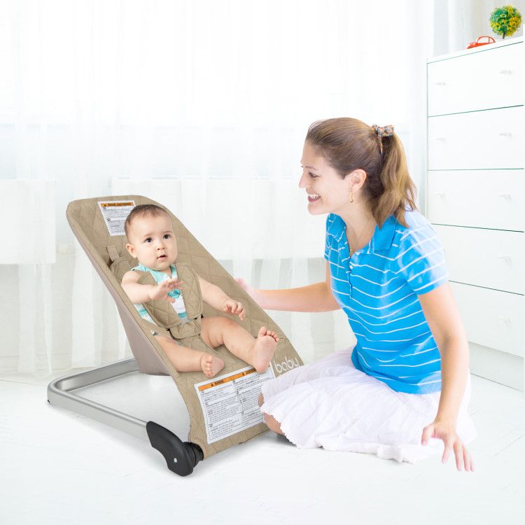 Baby bouncer seat with light beige cover and black base being used by a standing caregiver