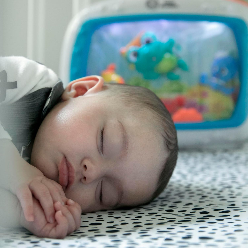 Baby sleeping beside blue crib toy and sound machine with sea-themed display