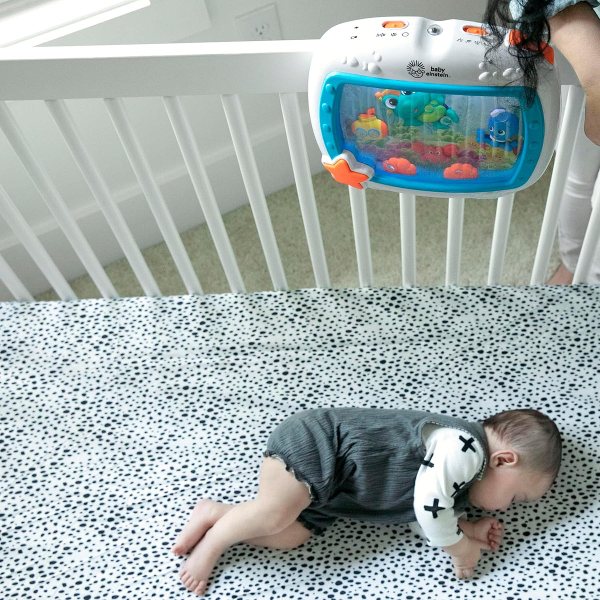 Infant lying on blanket in crib next to mounted blue ocean-screen sound machine