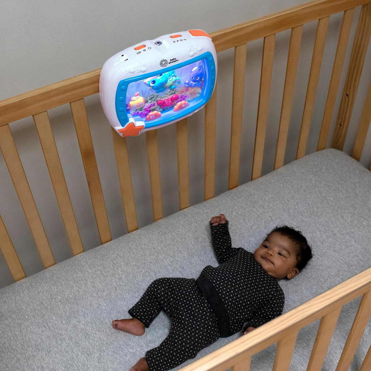 Sea Dreams sound machine on crib rail with glowing ocean screen and orange star button