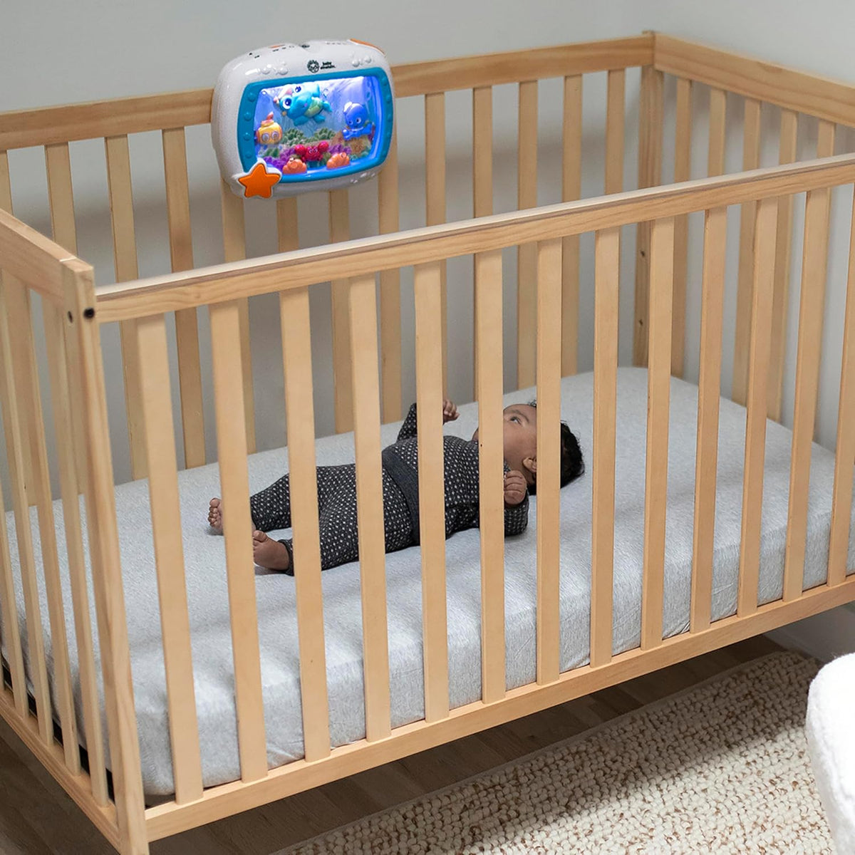 Infant in wooden crib with blue sea-themed sound machine mounted on railing