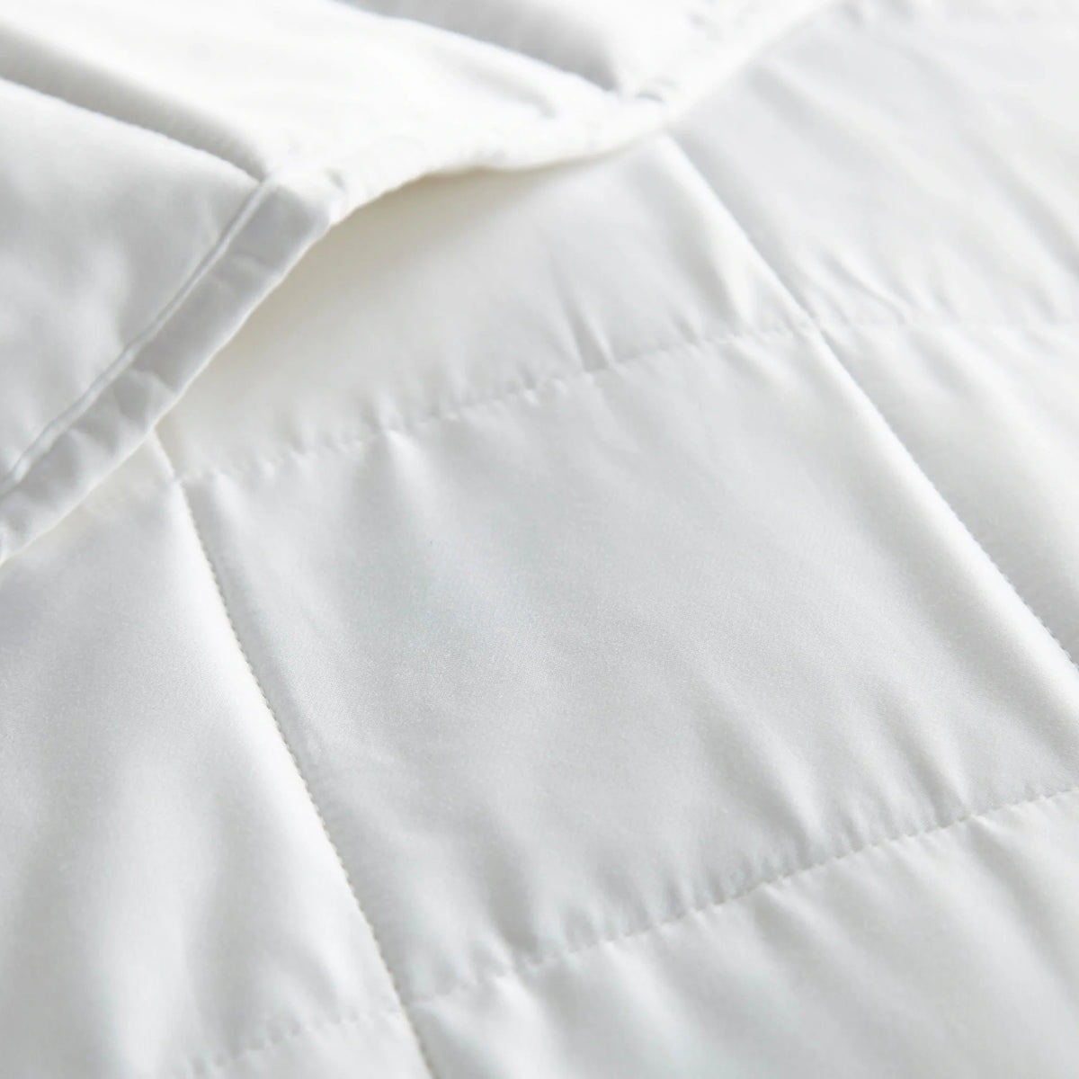 White duvet comforter fabric close-up with stitched quilt seam and channels