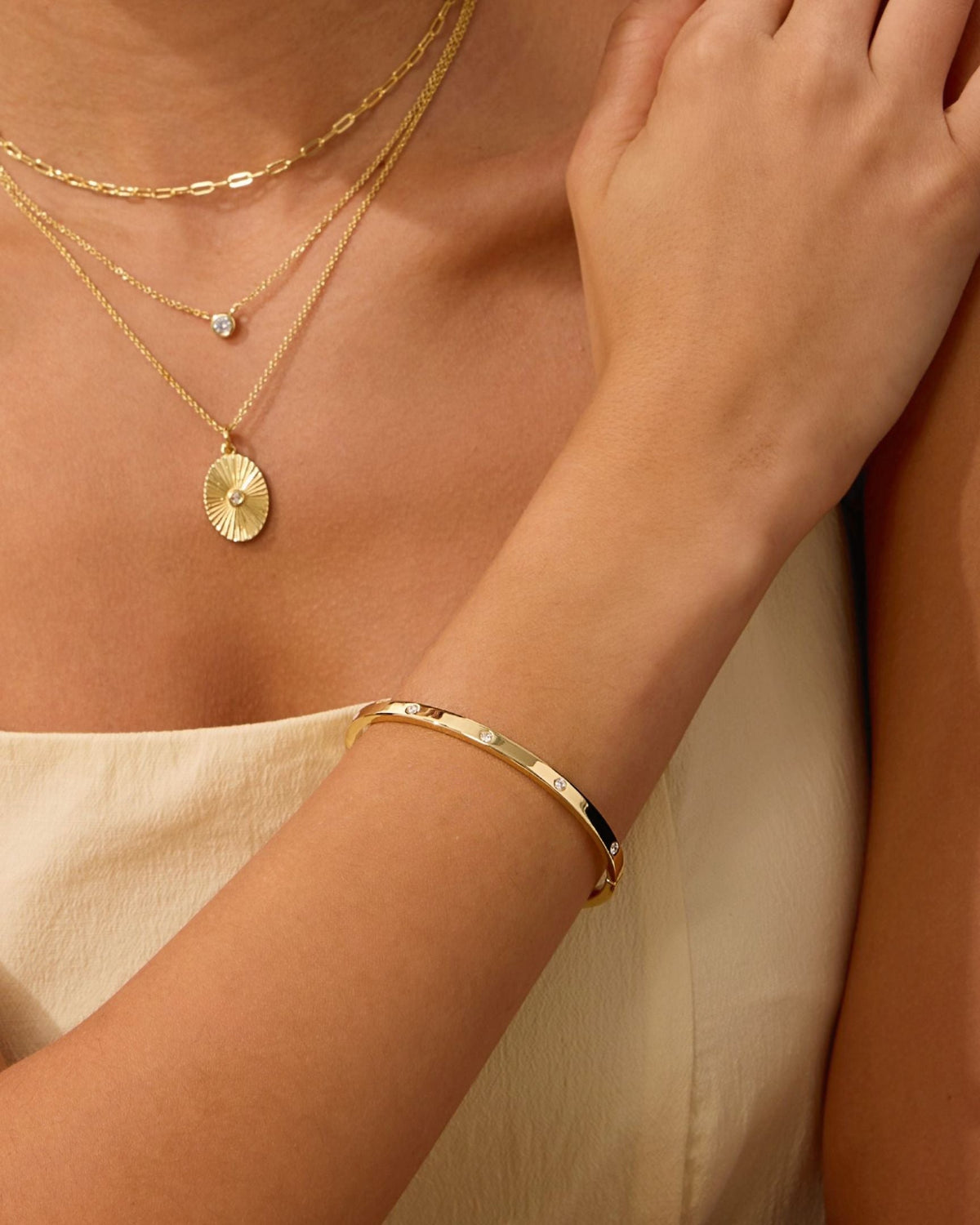 Gold-tone bangle cuff with small round diamond settings, worn with layered jewelry