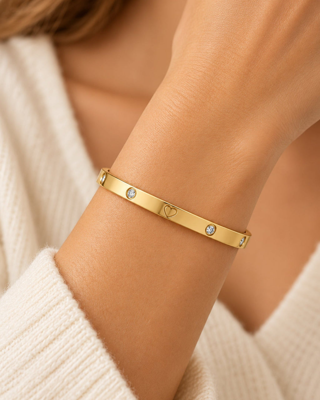 Gold-tone bangle with heart engraving and two small round stones on wrist