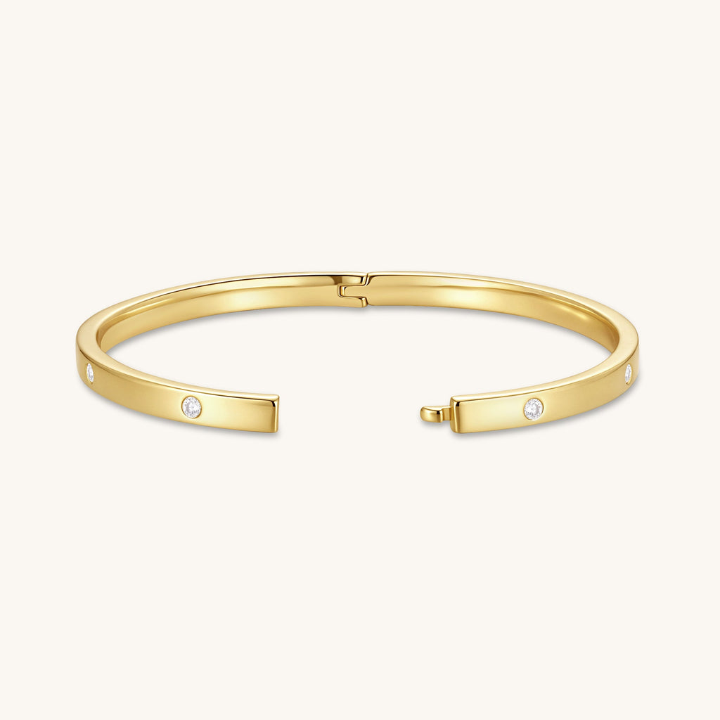 Gold-tone hinged bangle with round diamonds on the ends and center clasp, laid flat
