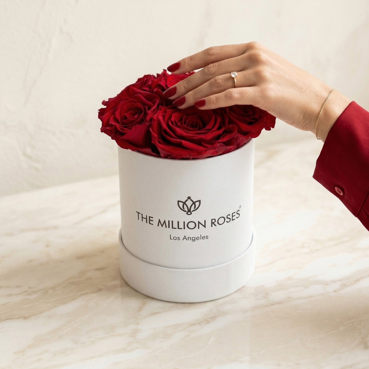 White cylindrical gift box with red roses, hand arranging the top