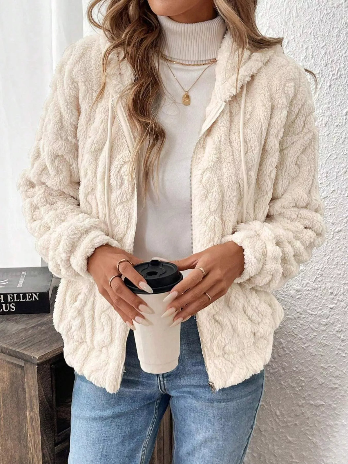 Ivory fleece zip-up hoodie with hood and drawstring, holding a black-lid tumbler