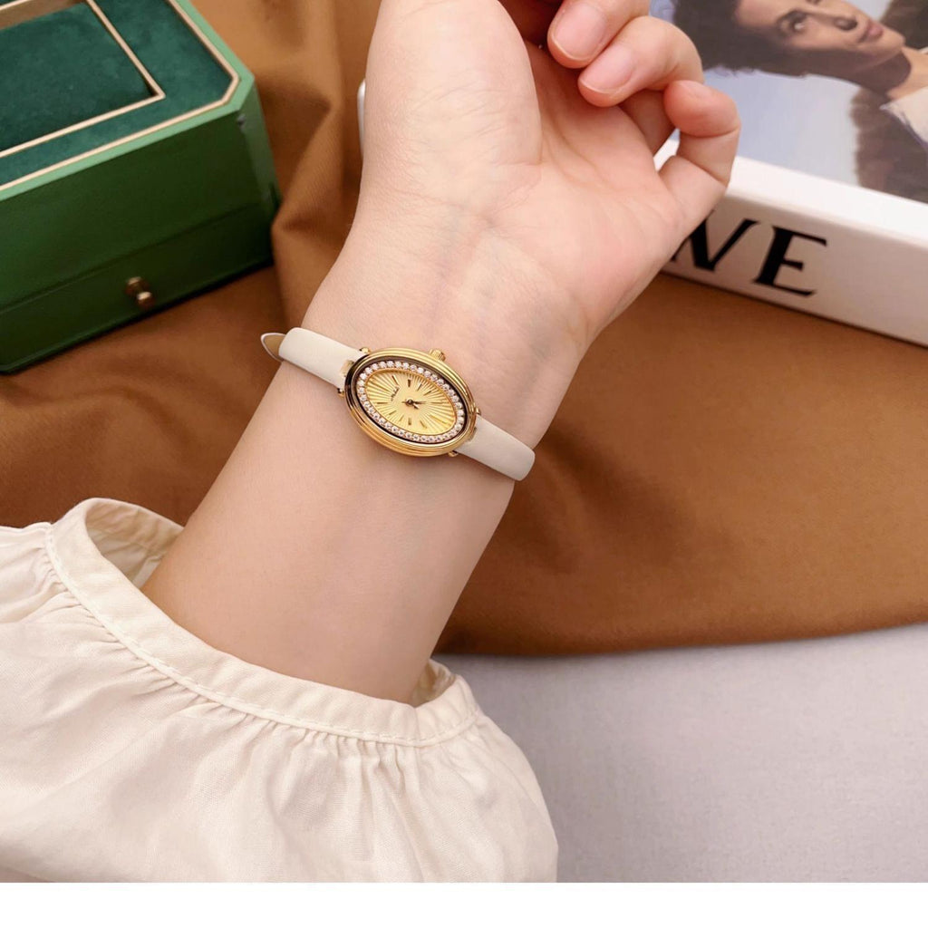 Ladies gold-tone wristwatch with yellow dial and white strap on a hand.