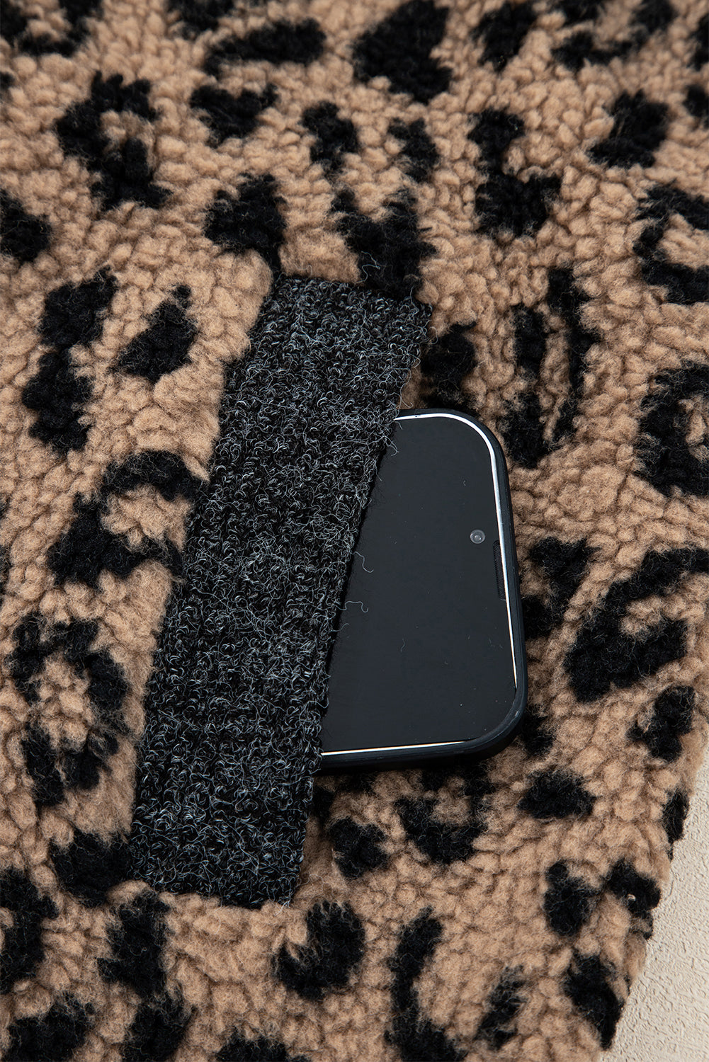 Leopard-print fleece side pocket holding a black phone, with zipper and dark pocket lining.