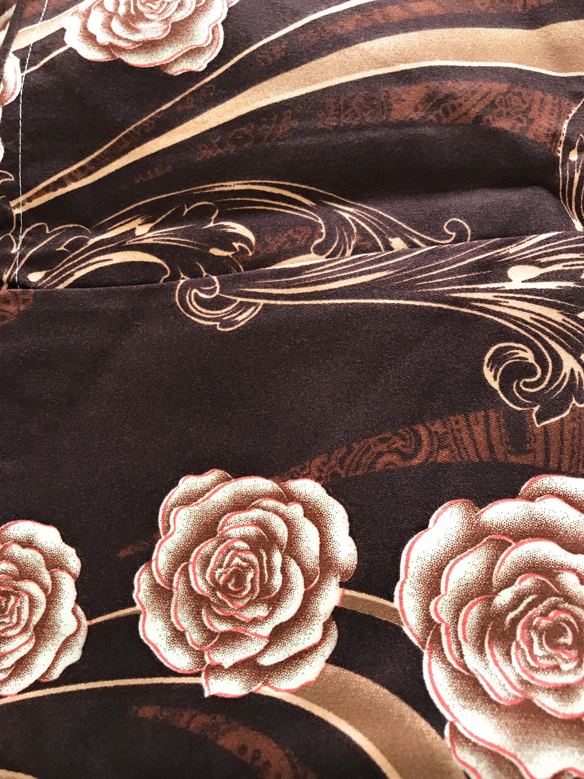 Brown bed sheet fabric close-up with gold swirls and rose floral pattern