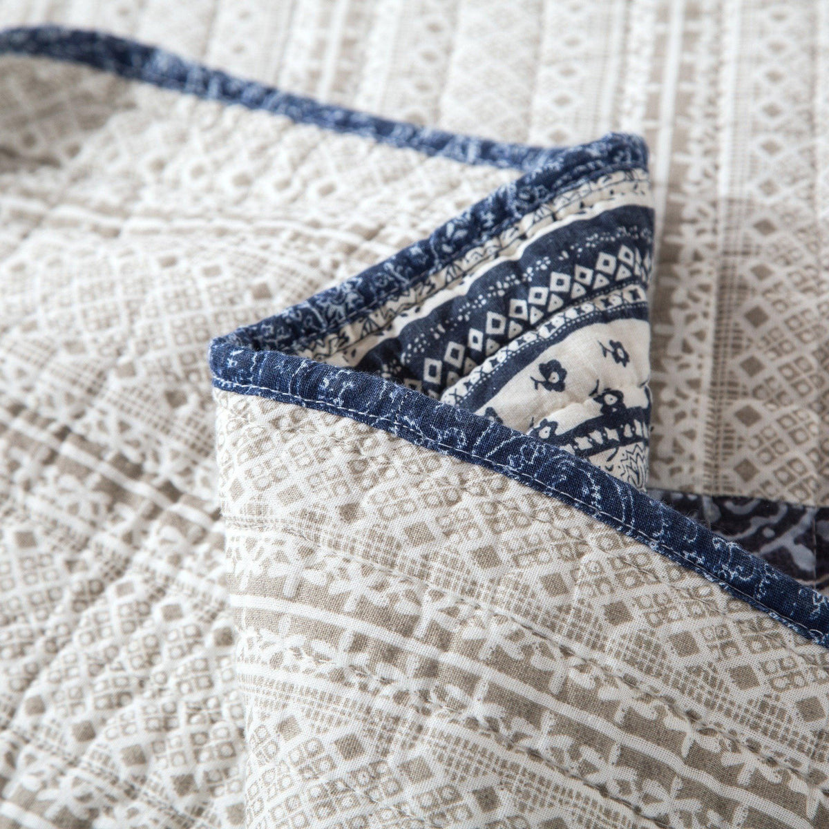 Close-up corner of denim blue patchwork quilt with stitched navy border