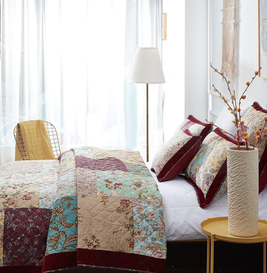 Patchwork quilt set with multicolor paisley blocks and burgundy trim on bed
