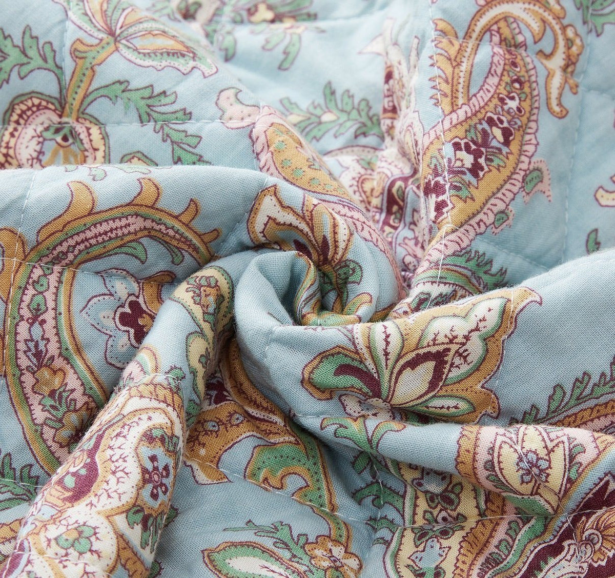 Cotton quilt fabric close-up with paisley floral print in teal and burgundy tones