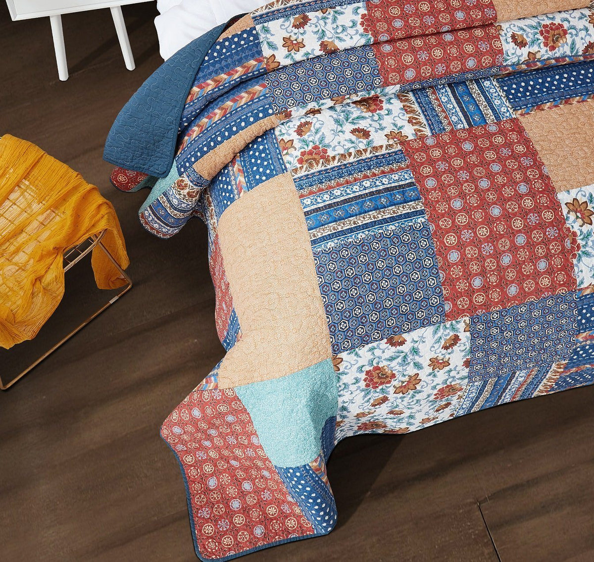 Corner view of quilted patchwork bedspread with blue, red, tan, and floral blocks