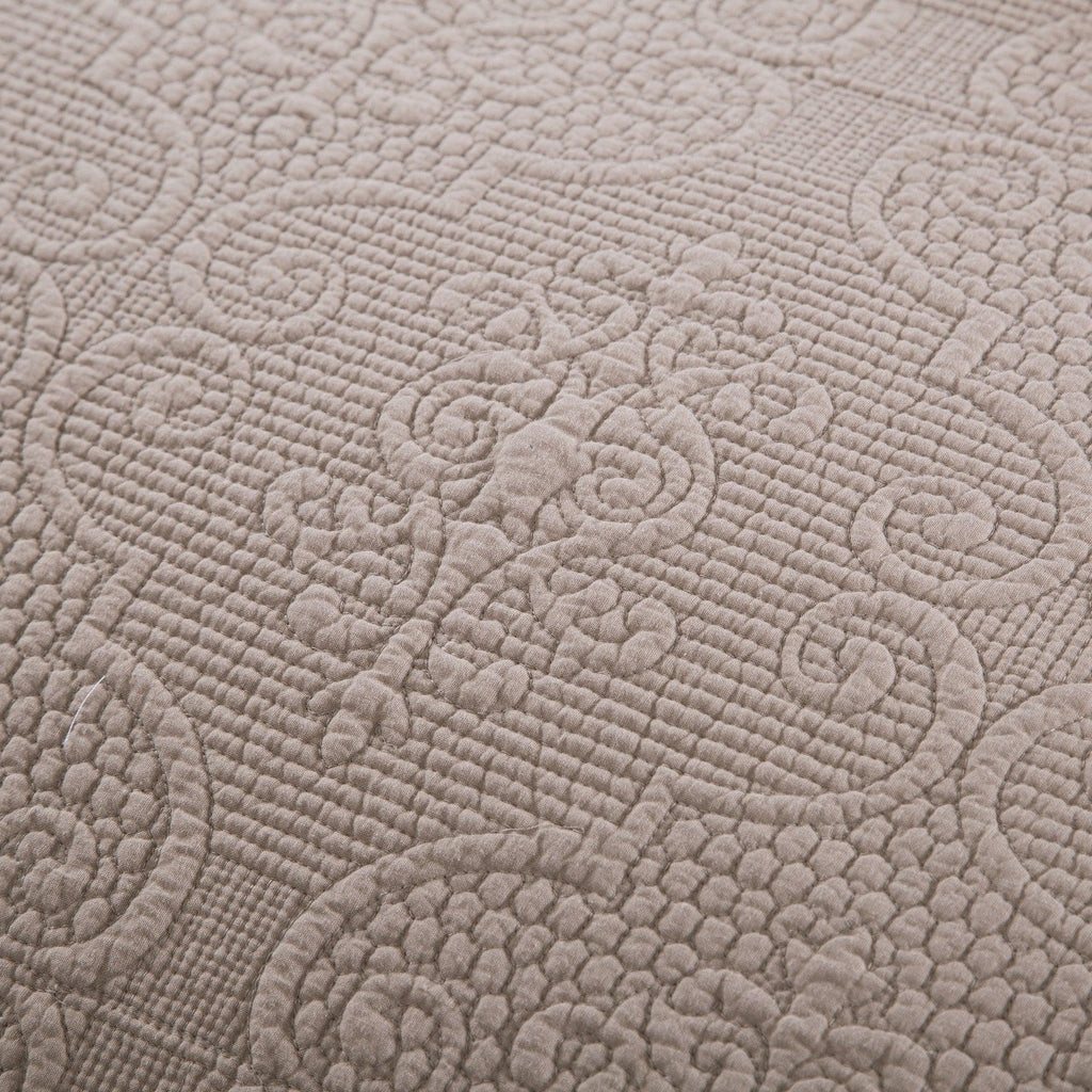 Close-up of quilted bedspread fabric with embossed swirl and textured quilting