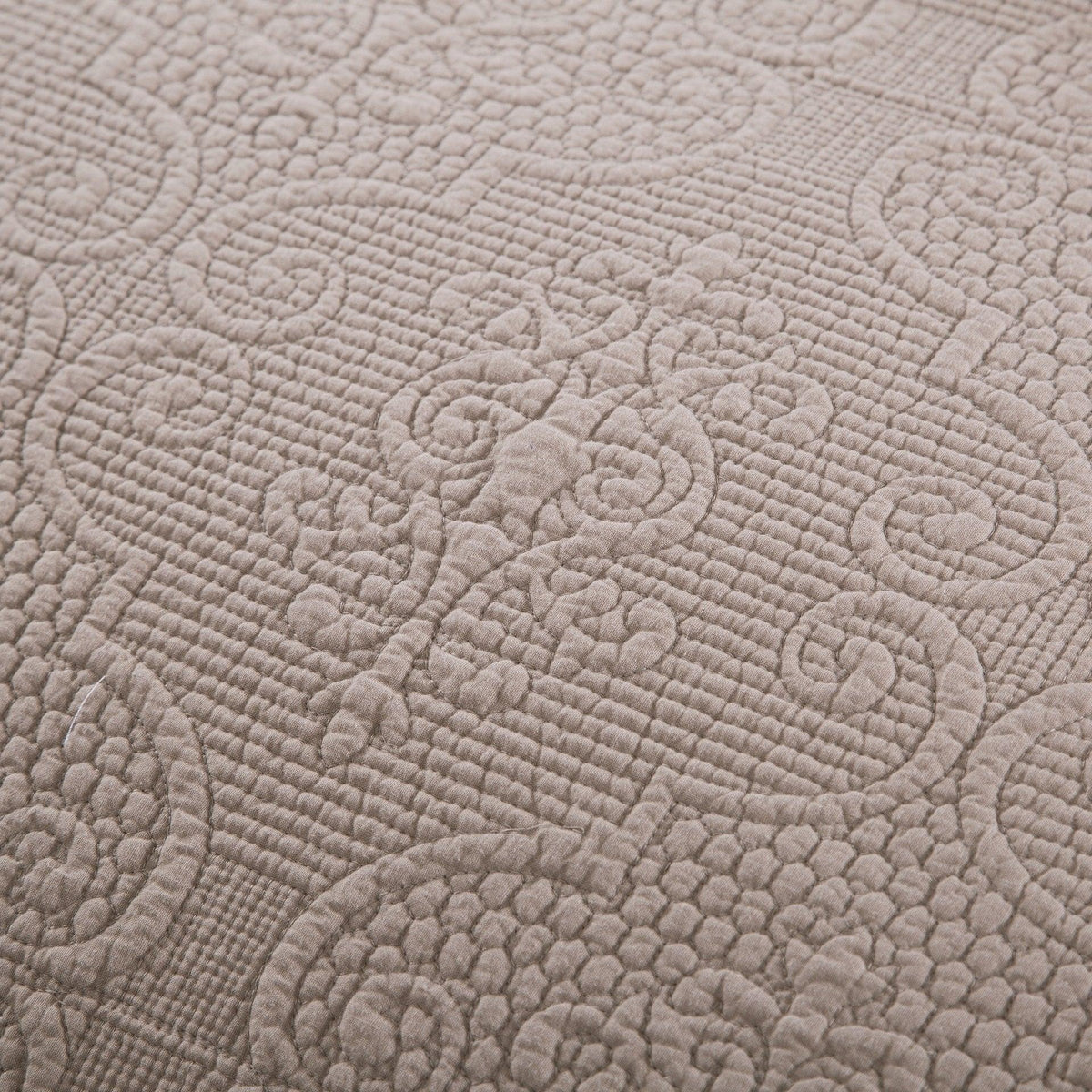 Close-up of quilted bedspread fabric with embossed swirl and textured quilting