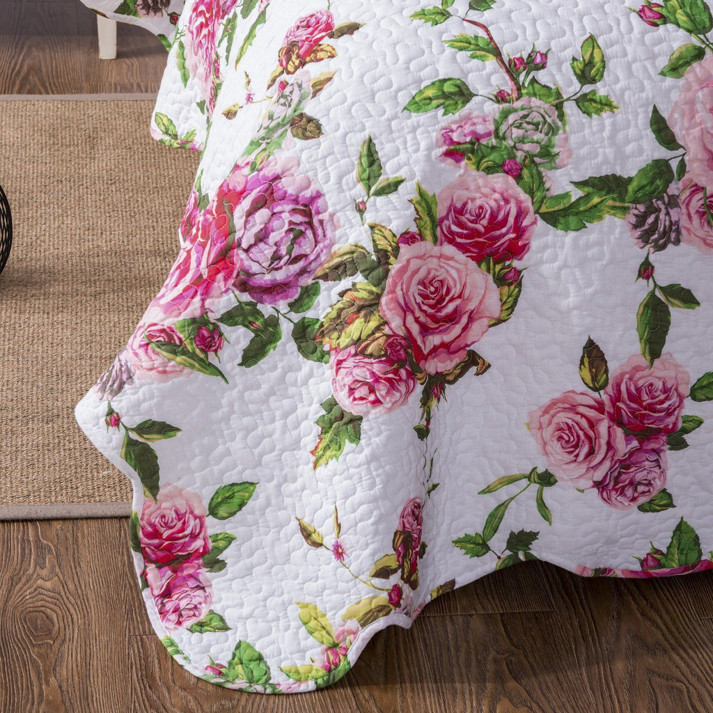 Corner close-up of white quilted fabric with pink rose floral pattern and green leaves