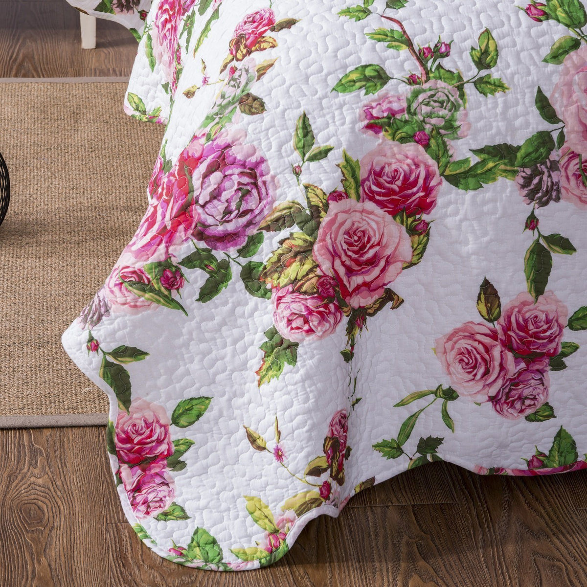 Corner close-up of white quilted fabric with pink rose floral pattern and green leaves