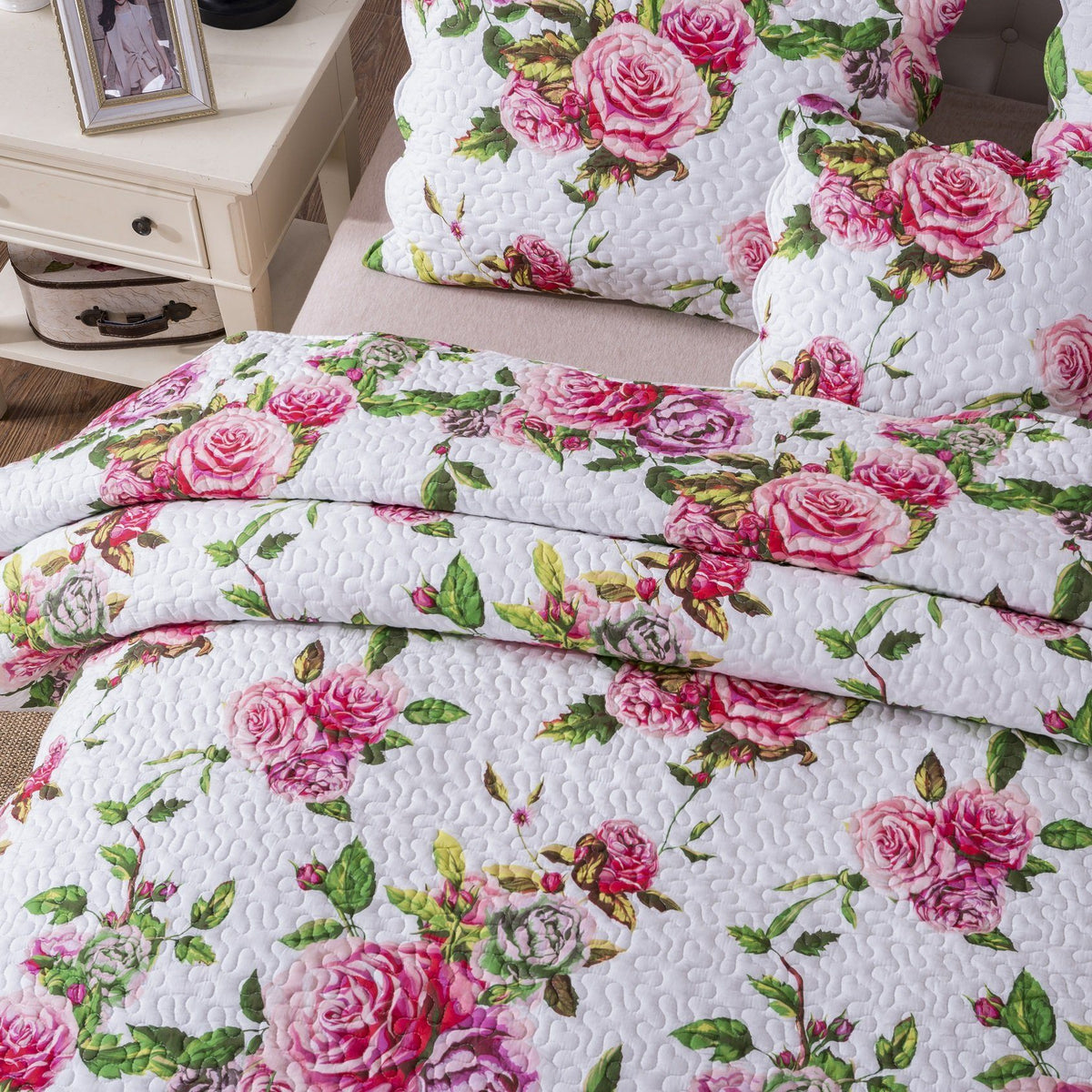 Folded quilted bedspread showing pink roses and green foliage on a white background