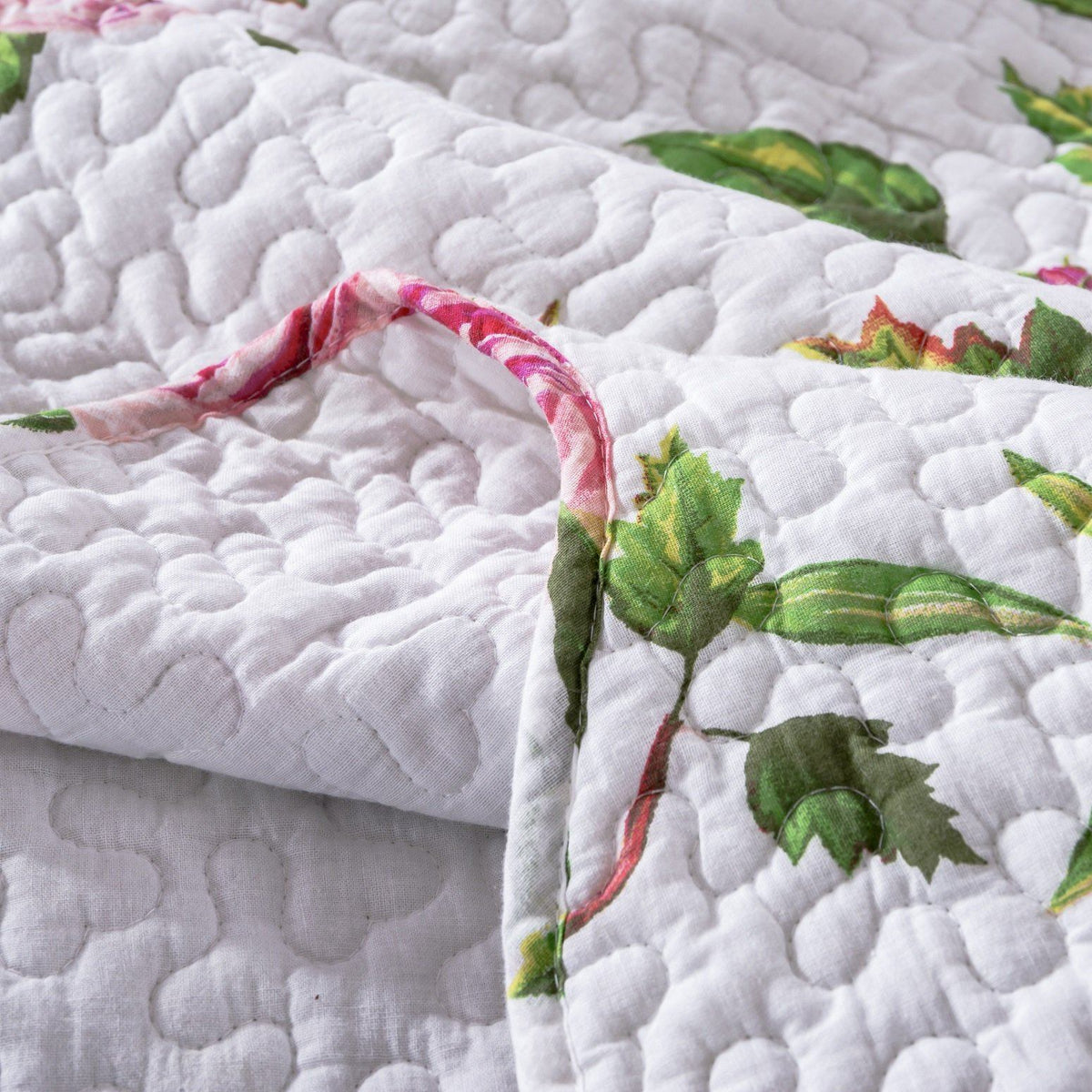 Close-up of white quilt fabric with textured quilting and pink rose pattern with leaves