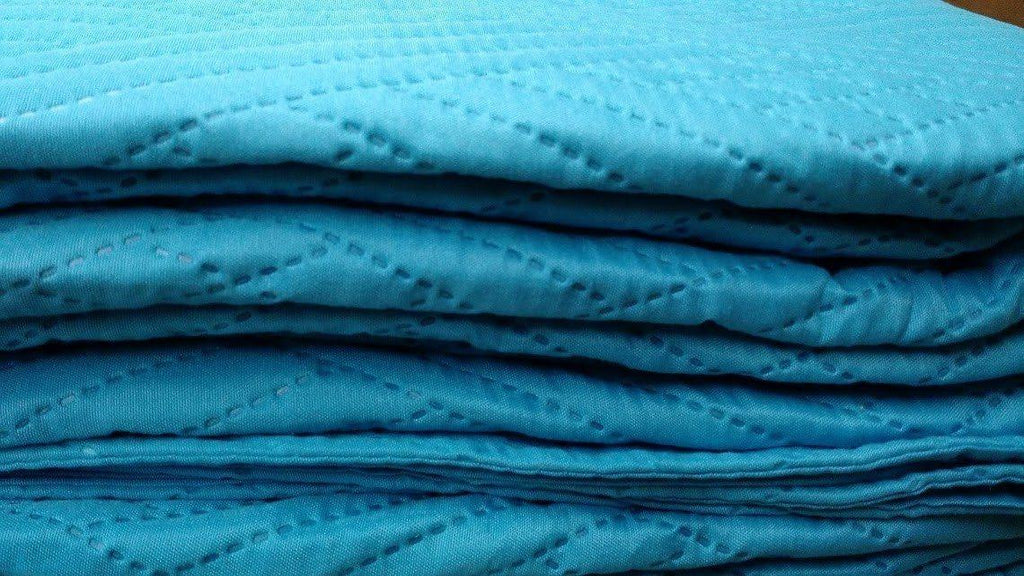 Turquoise teal quilted bedspread folded, showing layered wave-texture stitching