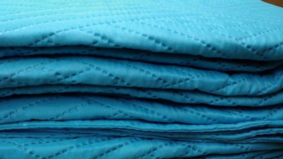 Turquoise teal quilted bedspread folded, showing layered wave-texture stitching