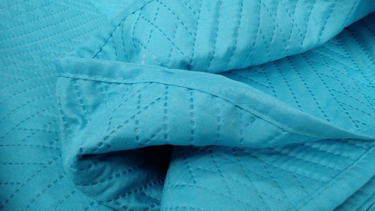Close-up of turquoise teal quilted bedspread seam with wave stitch quilting
